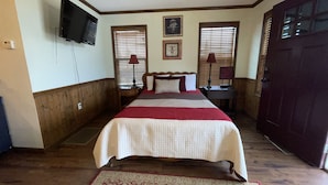 A bedroom with a bed, wooden flooring, a television mounted on the wall, and a door.