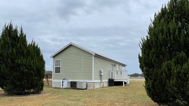 A single-story house with a front porch, a fenced yard, and two large evergreen trees.
