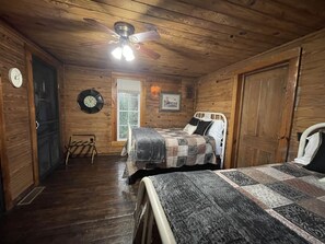 Un dormitorio de cabaña de madera con cama, una silla, un ventilador de techo, un reloj y una ventana.