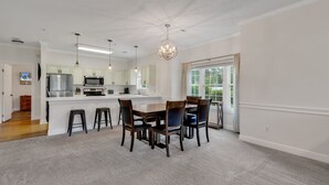 A modern kitchen with white cabinetry, a central island, and bar stools. - Elegant 3BR Condo: Magnolia North 101 (Myrtle Beach)