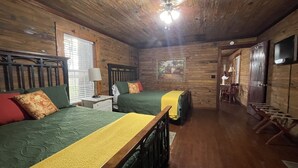 A wooden cabin-style room with two beds, a ceiling fan, and a television. - Row Cottages Redbud Cottage (Hartsfield)