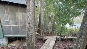 A wooden staircase leading to a cabin with a metal roof, surrounded by trees and a body of water. - Row Cottages Redbud Cottage (Hartsfield)