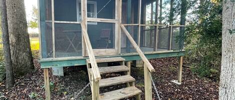 Eine Holzhütte mit einem Moskitonetz-Vorbau und einer Holztreppe, die davor hochführt.