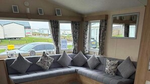 Un espacio habitable compacto con un sofá curvo, una mesita y una ventana con cortinas.