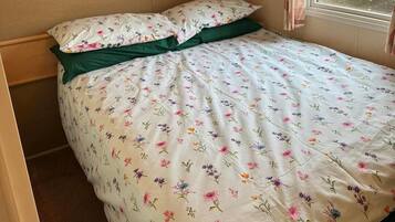 A bed with a floral-patterned bedspread and green pillows in a room with wooden cabinets and a window with curtains.
