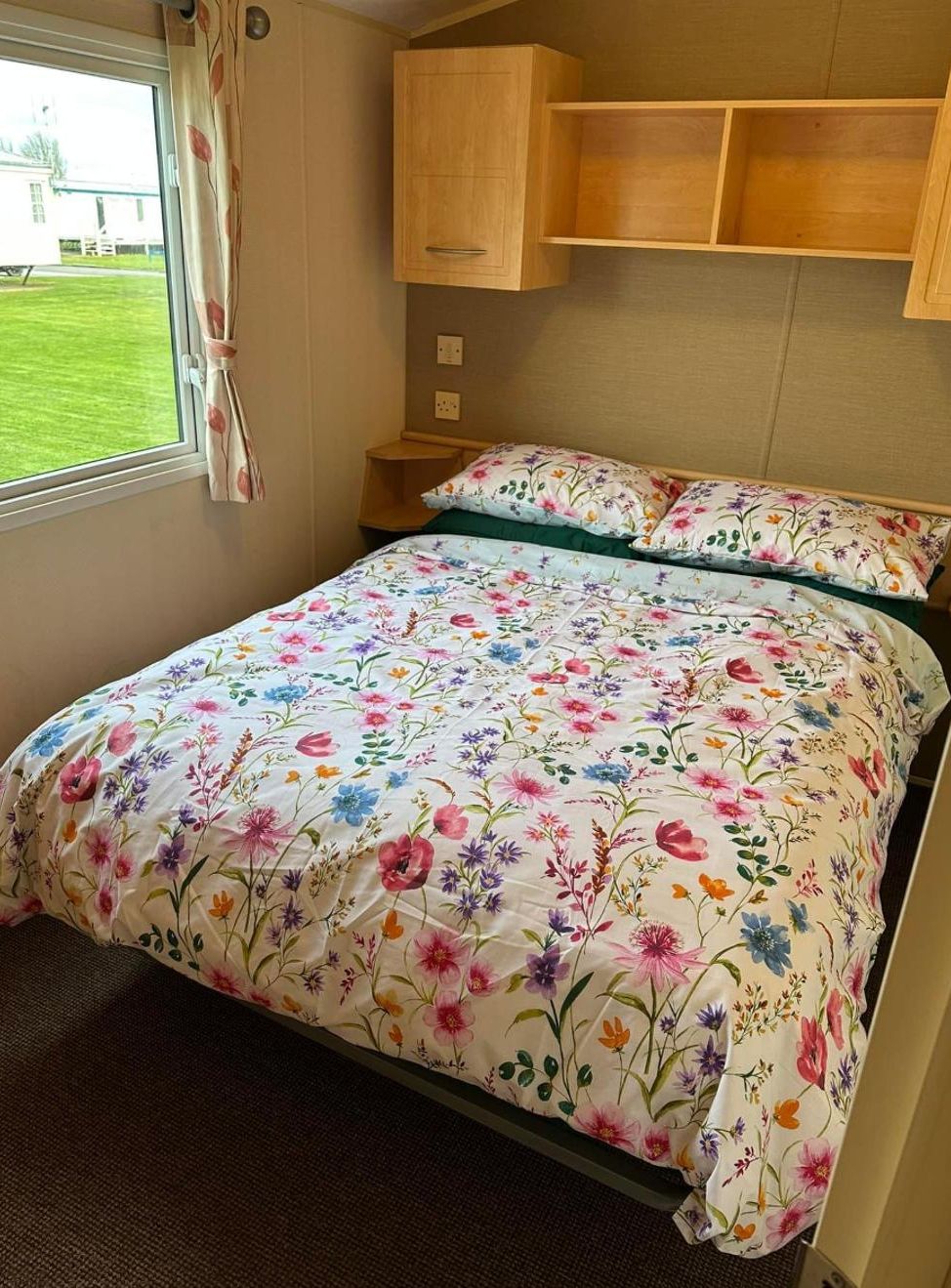 Un dormitorio con colcha estampada, cabecero de madera y ventana con cortinas.