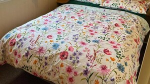 Un dormitorio con colcha estampada, cabecero de madera y ventana con cortinas.