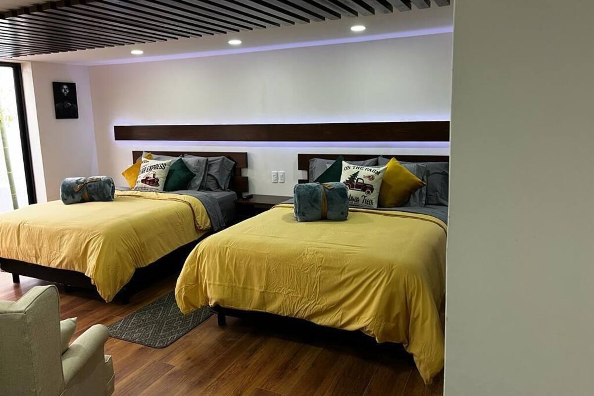 Une chambre d’hôtel avec deux lits, chacun recouvert d’une couvre-lit jaune et agrémenté de plusieurs oreillers. La chambre est dotée d’un plancher en bois et d’un plafond moderne avec un éclairage encastré.