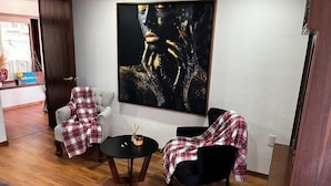 Ett modernt vardagsrum med en stor, abstrakt målning, två fåtöljer, ett litet runt bord och en soffa.