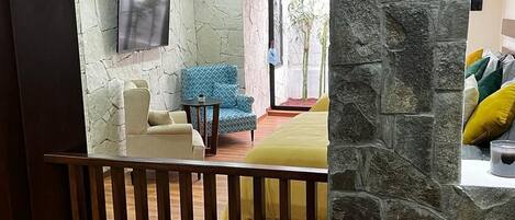 Una stanza con una parete in pietra, un letto con copriletto giallo, una poltrona blu con motivi e un tavolino.