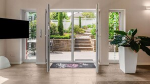 Una entrada moderna con puerta de cristal que da a un jardín. Se ven tres ventanas sobre la puerta, y una planta en maceta a la derecha.