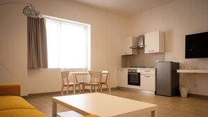 Una cocina moderna con armarios blancos, horno empotrado y refrigerador. Hay un comedor con mesa y sillas blancas.