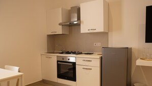 Cocina compacta con estufa, horno y refrigerador, armarios blancos y una pequeña mesa de comedor.