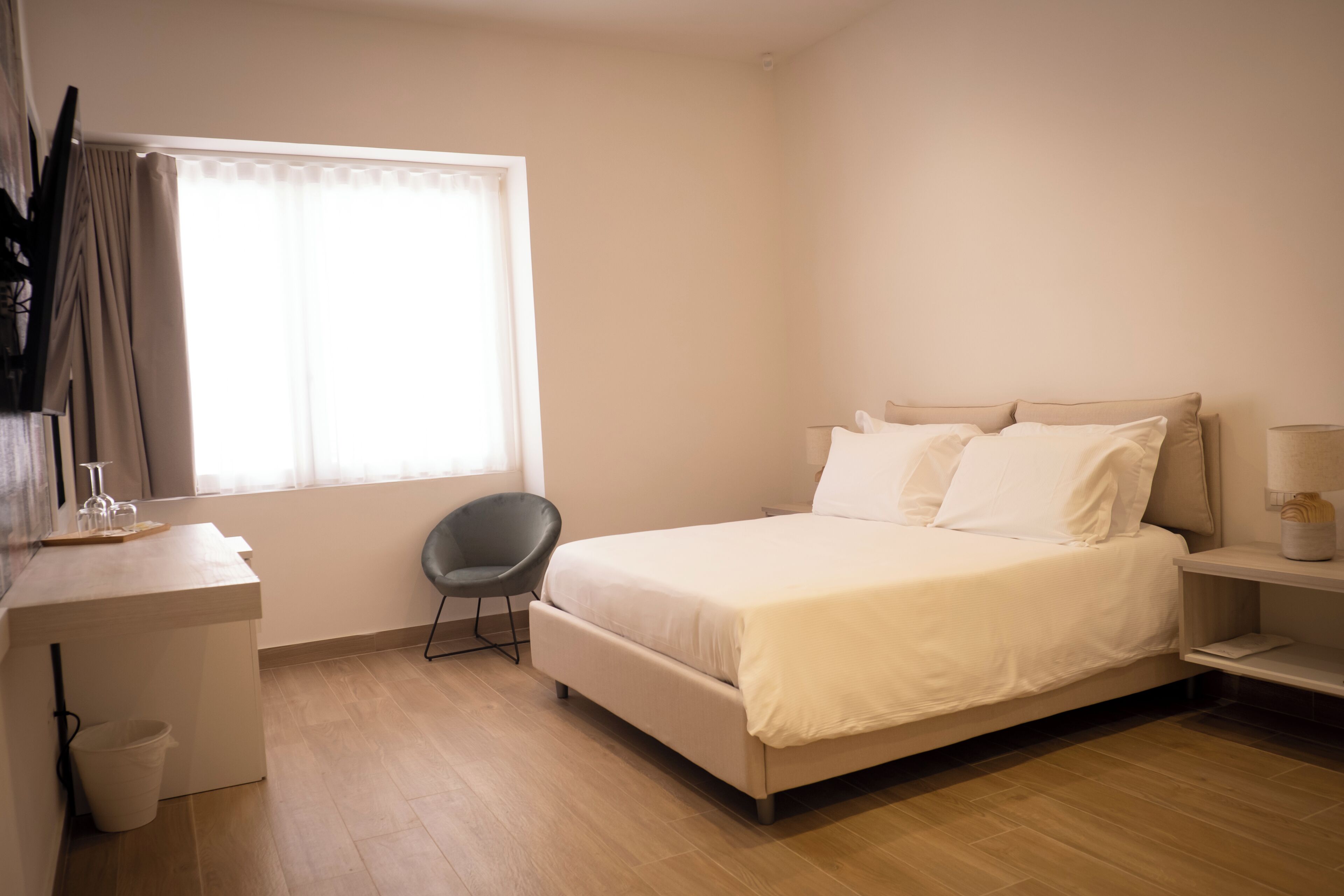 Un dormitorio con cama, escritorio, silla, ventana con cortinas y mesita de noche.