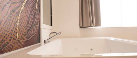 Un baño con una bañera grande, ducha y ventana con cortinas.