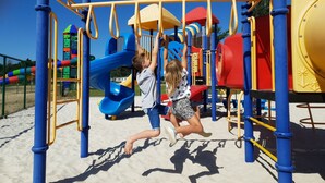 Un parque infantil con un tobogán, estructuras para escalar y una casita amarilla.