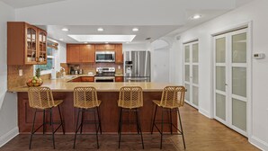 A modern kitchen with a central island, bar stools, and stainless steel appliances. - Palm Haus • Heated Pool • Near Beach • Game Room • Volleyball • Gas Fire Pit (Palm Harbor)