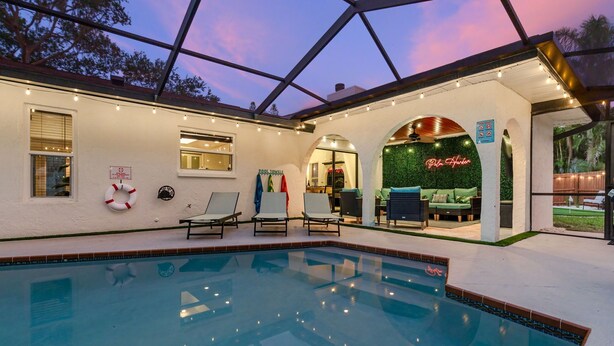 An indoor swimming pool with lounge chairs, a poolside bar, and a neon sign. - Palm Haus • Heated Pool • Near Beach • Game Room • Volleyball • Gas Fire Pit (Palm Harbor)