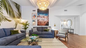 A modern living room with a large sofa, a coffee table, and a chandelier. - Palm Haus • Heated Pool • Near Beach • Game Room • Volleyball • Gas Fire Pit (Palm Harbor)