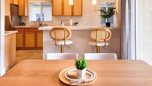 Una cocina moderna con armarios de madera, una mesa de comedor con dos sillas y lámparas colgantes.