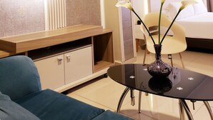 A modern hotel room with a round mirror, a bed, a bedside table, a vase with flowers, and a blue sofa. - HOTEL SUITE CENTER (Pereira)