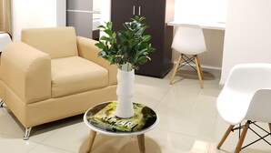 A modern living room with a beige sofa, a white armchair, a round coffee table with a plant, and a dark-colored wardrobe. - HOTEL SUITE CENTER (Pereira)