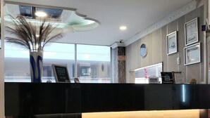 A reception area with a black counter, a wooden panel, a clock, framed certificates, and a large window. - HOTEL SUITE CENTER (Pereira)