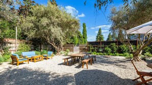 An outdoor seating area with a table and benches, surrounded by trees and a gravel ground. - Jasmine residence, located downtown between the Union Hotel & Bells restaurant. (Los Alamos)
