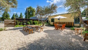 An outdoor patio area with a gravel surface, wooden tables and benches, and a covered seating area with a table and chairs. - Jasmine residence, located downtown between the Union Hotel & Bells restaurant. (Los Alamos)