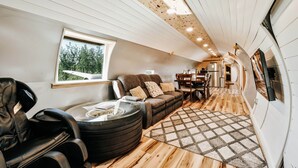 Et moderne interiør med træloft, massagestol, sofa, spisebord og udsigt gennem et vindue.