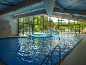An indoor swimming pool with clear glass walls, a slide, and a small play area. - Studio Chalet in a Holiday Park (Ruinen)