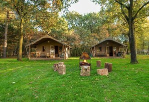 Two rustic cabins with wooden decks, surrounded by trees and a central fire pit. - Studio Chalet in a Holiday Park (Ruinen)