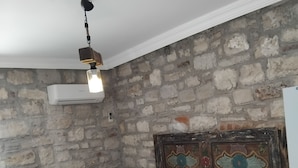 Een kamer met een stenen muur, een bed met wit en bruin beddengoed, een plafondventilator en een airconditioning.