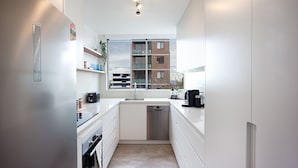 A modern kitchen with white cabinets, a built-in dishwasher, a window with a view of a brick building, and a coffee maker on the counter.
