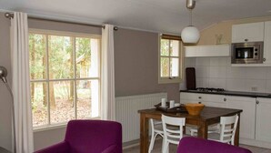 A modern kitchen with white cabinets, a built-in oven, and a dining area with a wooden table and purple chairs. - Cozy Chalet Near a National Park (Ruinen)