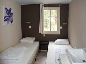 A room with two single beds, a window with curtains, a small desk, and a wall-mounted light fixture. - Cozy Chalet Near a National Park (Ruinen)
