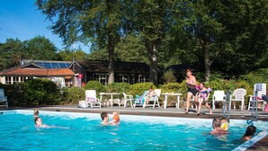 A swimming pool with people in the water, surrounded by lounge chairs and a building with a tiled roof. - Cozy Chalet Near a National Park (Ruinen)