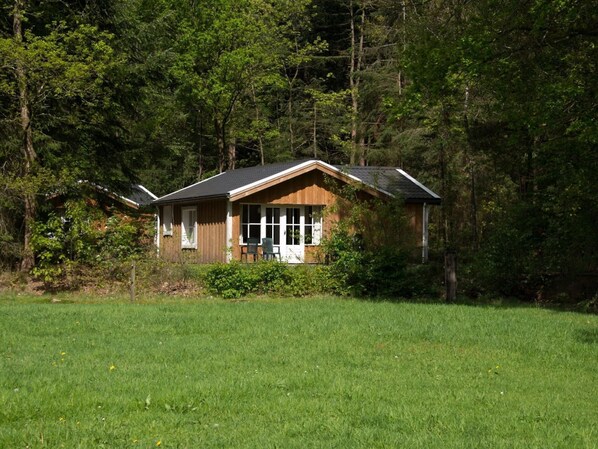 A cabin with a sloped roof, large windows, and a porch with a chair. - Cozy Chalet Near a National Park (Ruinen)