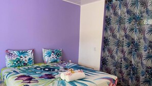 Een bed met bloemenbeddengoed, een paarse wand en een gordijn met een tropisch dessin.