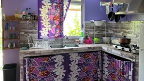 Een keuken met paarse accenten, voorzien van een spoelbak, kookplaat en hangende pannen.