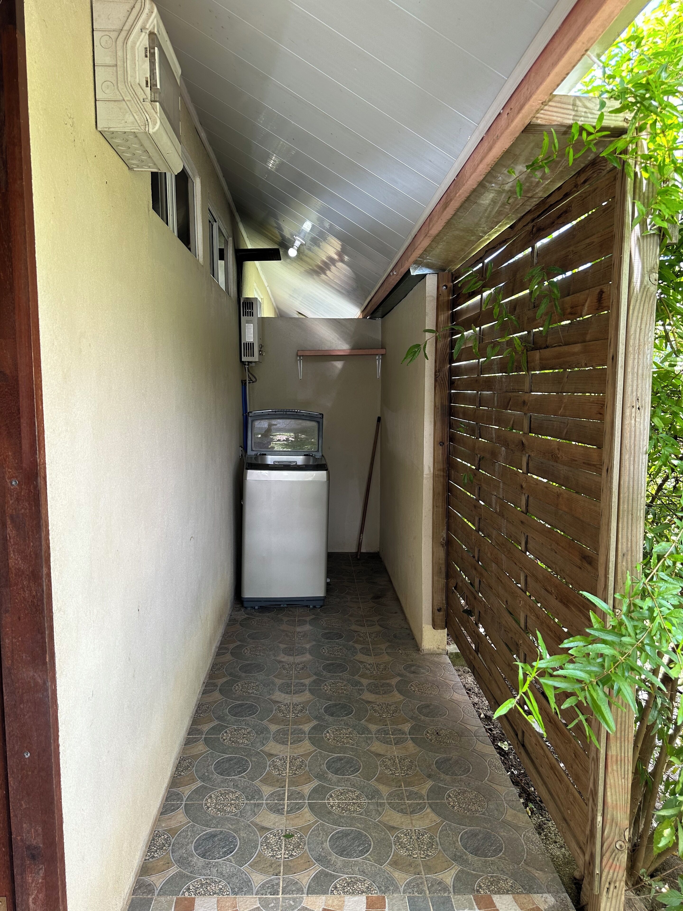 A narrow hallway with a washing machine, a ceiling fan, and a wooden fence on one side.