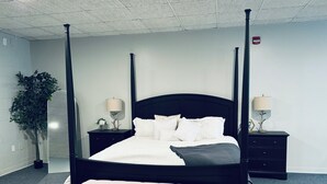 A four-poster bed with a bench in front, two bedside tables with lamps, a potted plant, and a fire alarm on the wall.
