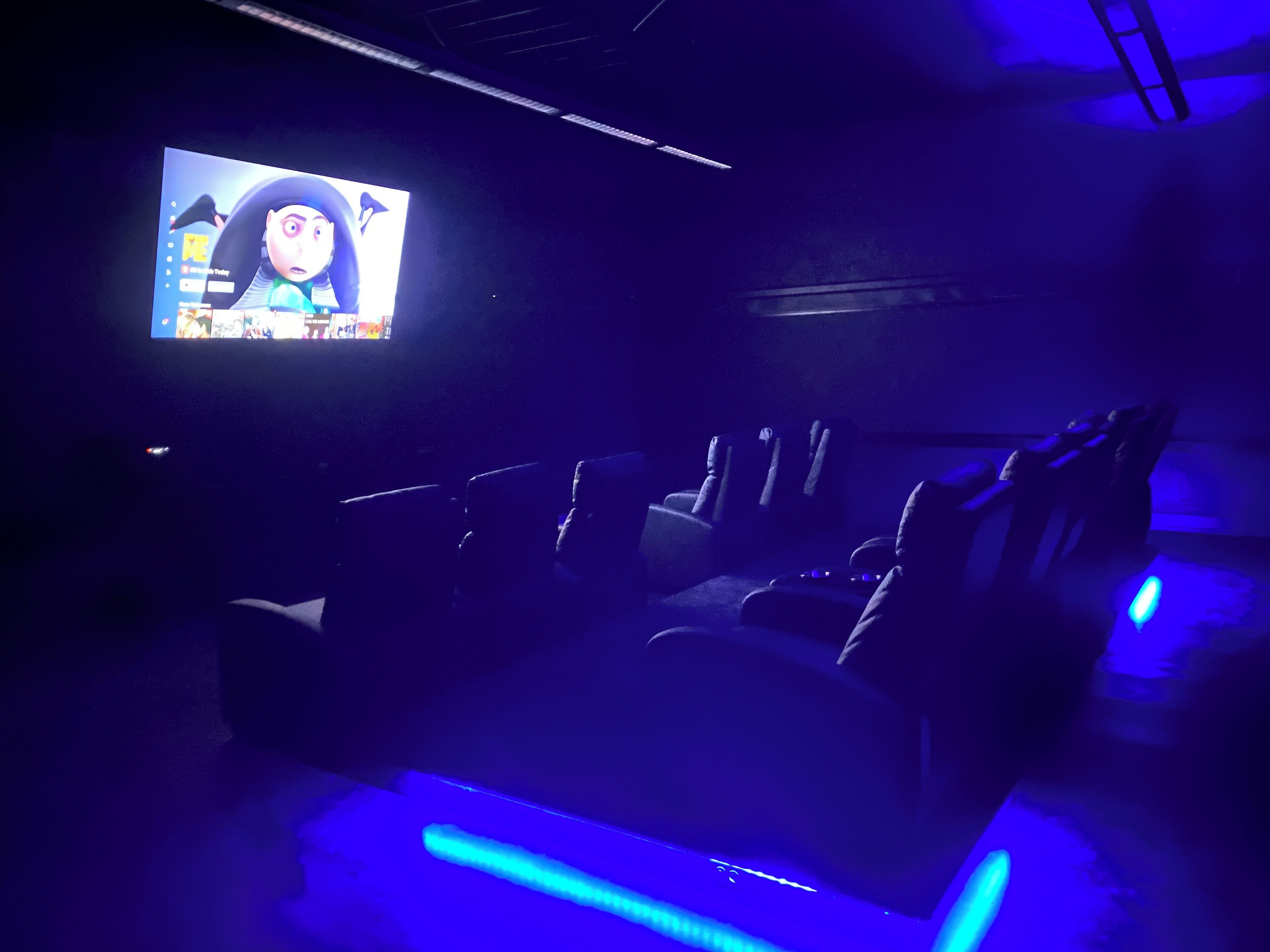 A dark room with a large screen displaying a cartoon character, rows of seats, and blue ambient lighting.