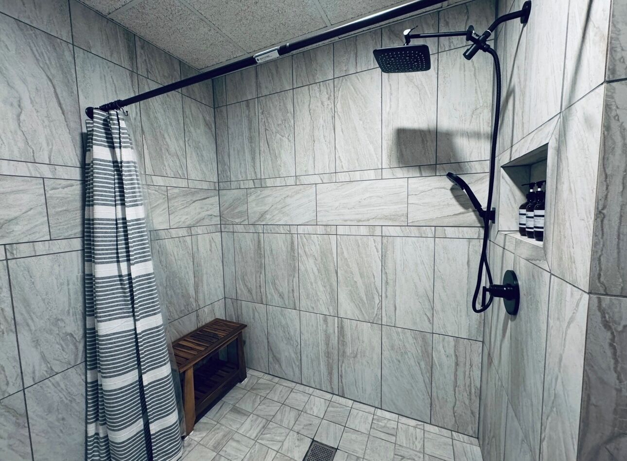 A shower area with a curved showerhead, a handheld showerhead, and a shower curtain.
