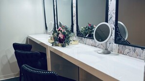 A room with a vanity table, three mirrors, and two black chairs.