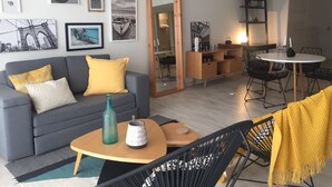 Ein modernes Wohnzimmer mit einem grauen Sofa, gelben Kissen, einem Couchtisch und einem Essbereich mit einem runden Tisch und Stühlen.