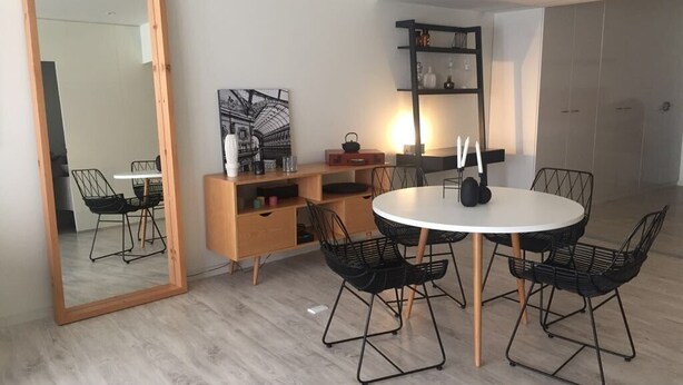 Ein moderner Essbereich mit einem runden Tisch, schwarzen Stuhlgestellen aus Draht, einer Holzsideboard und einem großen Spiegel.