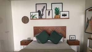 Ein Schlafzimmer mit einem Bett, zwei Nachttischen, einem hölzernen Kopfteil und gerahmten Bildern an der Wand.
