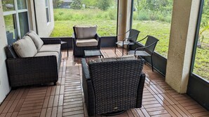 Eine überdachte Terrasse mit Korbmöbeln und großen Fenstern, die Blick auf eine Rasenfläche bietet.