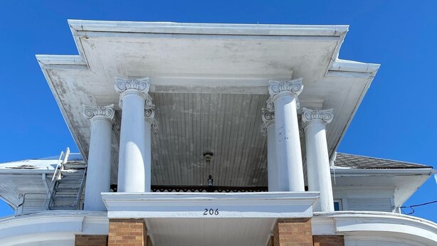 Un bâtiment à deux étages doté d’une entrée centrale, d’une façade en briques et d’un porche blanc orné de colonnes.